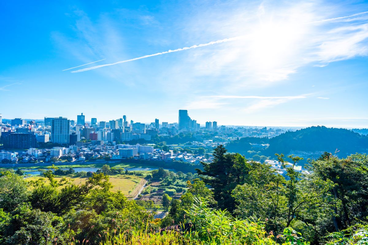 青空と広がる仙台市の風景、手前には緑豊かな森林と田園が広がる。清々しい自然と都会が共存する美しい眺め。