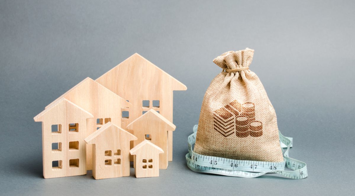 住宅ローンや不動産投資の費用評価をイメージさせる、木製家模型とお金の袋、メジャー。